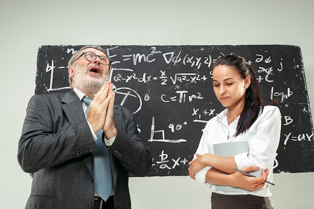 Professeur senior masculin et jeune étudiante contre tableau en classe. Notion d'émotions humaines. Modèles caucasiens. Éducation, collège, université, conférence, école, concepts d'apprentissage