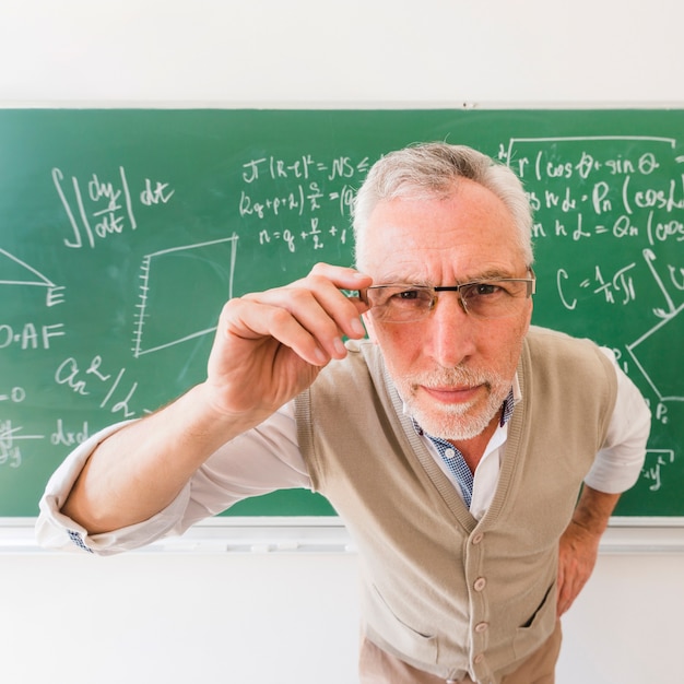 Professeur senior regardant à travers des lunettes à la caméra