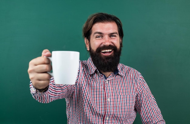 Professeur d'université boit du café après la leçon de retour à l'école journée de la connaissance de l'éducation formelle enseignant barbu mature à la leçon homme brutal travail en classe avec tableau noir se prépare à l'examen