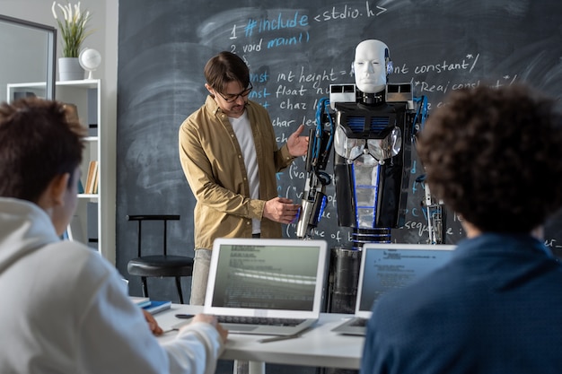 Professeur d'université technique debout par robot d'automatisation par tableau noir tout en présentant l'innovation à un groupe d'étudiants au séminaire