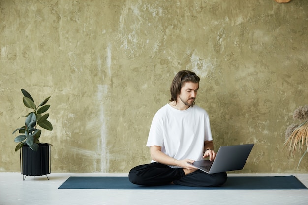 Professeur de yoga à l'aide d'un ordinateur portable assis en posture de lotus, pratique de la médiation à distance, espace copie, concept de santé mentale