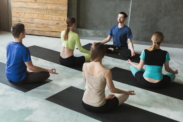 Professeur de yoga et débutants en classe, faisant des exercices d'asanas. Posture du lotus. Mode de vie sain dans un club de fitness. Stretching avec coach, vue de dos