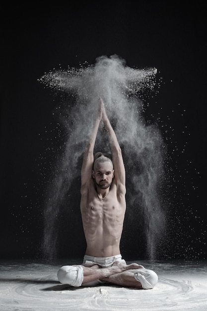 Un professeur de yoga est assis dans un sukhasana sur fond noir