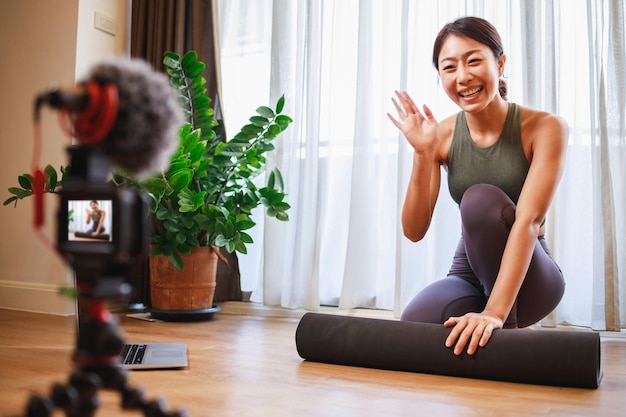 Professeur de yoga femme asiatique filmant un cours de yoga en ligne sur vidéo pour les médias sociaux Instructeur professionnel en vêtements de sport posant sur une caméra vidéo Technologie de mode de vie sain à la maison Nouveau mode de vie normal