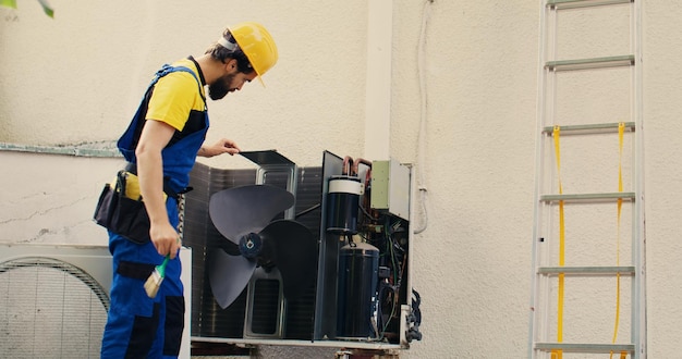 Professionnel compétent chargé par le client de réparer le climatiseur cassé à l'aide d'une brosse à épousseter douce pour éliminer la couche accumulée de saleté et de poussière qui ralentit les composants internes