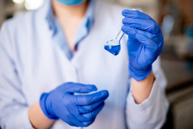 Professionnel de la science féminine focalisée tenant une solution bleue dans la cuvette en verre