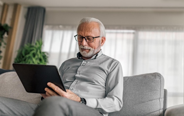 Professionnel senior utilisant une tablette numérique assis sur un canapé au bureau à domicile