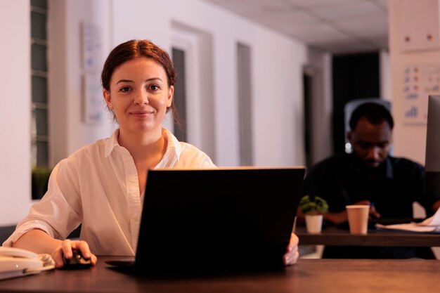 Professionnel souriant utilisant un ordinateur portable au bureau, regardant la caméra, femme tapant sur un portrait d'ordinateur. Employé d'entreprise naviguant sur le site Web au bureau du lieu de travail, analysant le rapport marketing