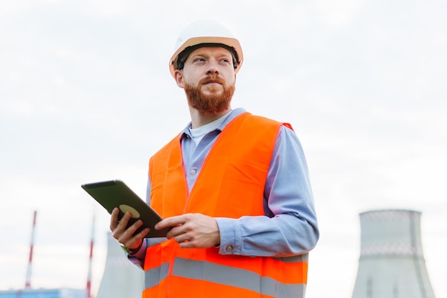 Un professionnel à succès L'homme est un ingénieur dans un casque et un gilet de protection orange Tablette à la main