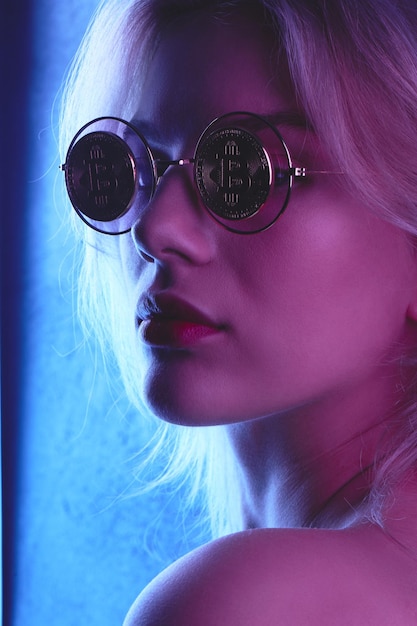 Profil d'une belle jeune femme blonde aux lèvres rouges dans des verres avec des bitcoins en ton bleu rouge. Concept de crypto-monnaie