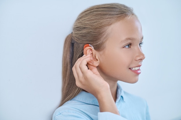 Profil de fille touchant l'oreille avec une prothèse auditive