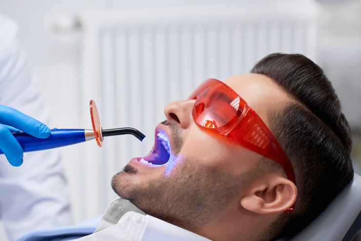 Photo profil gros plan d'un bel homme barbu portant des lunettes de protection obtenir le remplissage des dents fait à sa clinique dentaire copyspace technologie lampe ultraviolette uv médecine moderne santé.