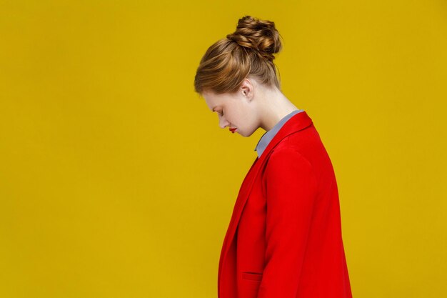 Profil inquiète femme rousse en veste rouge nerveuse. Studio shot, isolé sur fond jaune