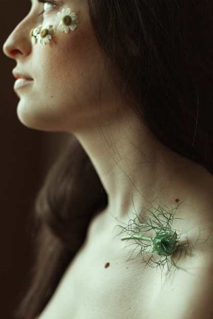 Profil d'une jeune brune avec de petites marguerites sur ses joues et une tige verte sur sa clavicule.