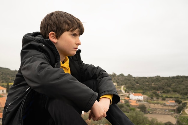Profil d'un jeune garçon sérieux envisageant de s'asseoir dans la montagne près d'une ville