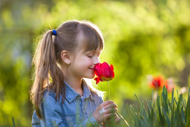 Profil de la jolie fille enfant souriante aux yeux gris et aux cheveux longs qui sentent la fleur de tulipe rouge vif