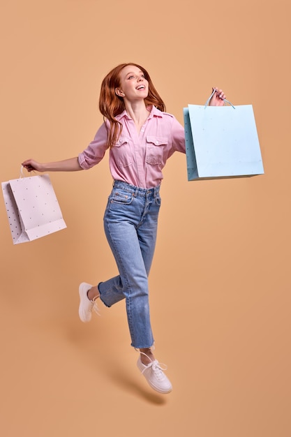 Profitant de l'achat d'une dame élégante et excitée, rentre chez elle après des achats réussis tenant de nombreux packs isolés sur fond de studio jaune beige avec espace de copie