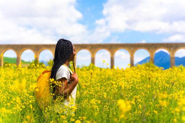 Profitant du printemps fille ethnique noire avec des tresses voyageur dans un champ de fleurs jaunes