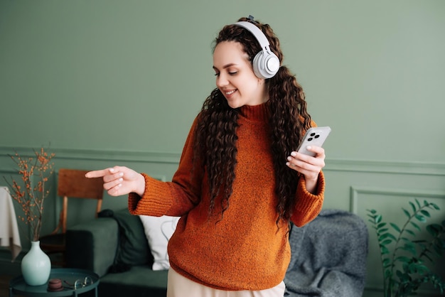 Profiter des battements femme dansant sur de la musique au téléphone avec des écouteurs dans le salon femme heureuse