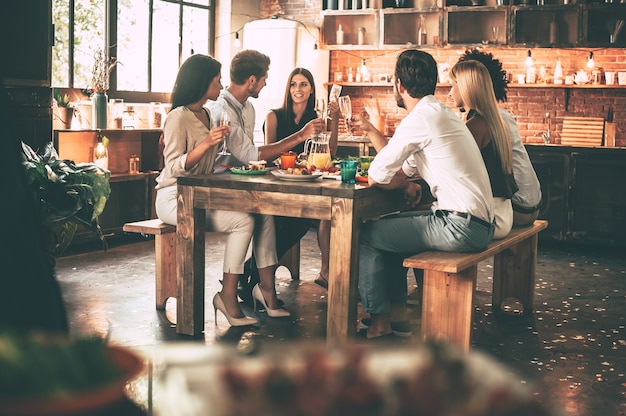 Profiter d'un dîner avec des amis. Groupe de jeunes joyeux dînant assis ensemble dans la cuisine