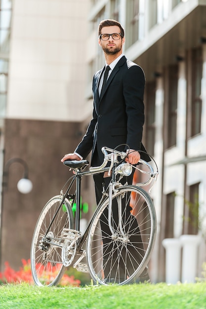 Profiter du mode de vie urbain. Faible angle de vue d'un jeune homme d'affaires confiant regardant loin et tenant la main sur son vélo tout en se tenant à l'extérieur