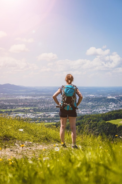 Profiter du paysage de montagne idyllique de Gaisberg Girl se tient sur une prairie idyllique et profite de la vue sur la ville lointaine de Salzbourg