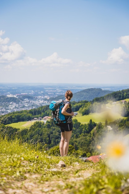 Profiter du paysage de montagne idyllique de Gaisberg Girl se tient sur une prairie idyllique et profite de la vue sur la ville lointaine de Salzbourg