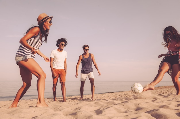 Profiter du temps avec des amis. Groupe de jeunes joyeux jouant avec un ballon de football sur la plage