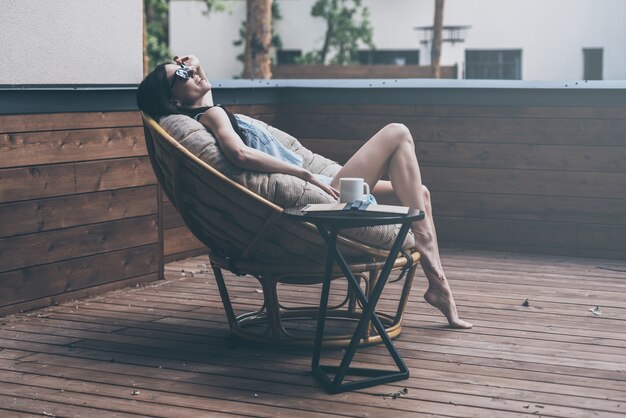 Profiter du temps sans soucis. Belle jeune femme se reposant dans une grande chaise confortable sur sa terrasse extérieure de maison