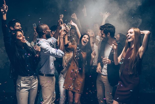 Profiter du temps sans soucis ensemble. Groupe de beaux jeunes jetant des confettis colorés et ayant l'air heureux