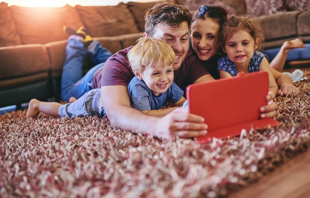 Profiter ensemble d'un film familial Photo d'une jeune famille heureuse regardant une tablette ensemble allongée sur le tapis de son salon