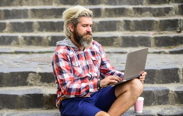 Profiter de la vie étudiante Homme d'affaires utilisant un ordinateur portable à emporter du café Échappé du bureau entrepreneur prospère homme mûr assis dans les escaliers avec un ordinateur portable et vérifiant les e-mails homme travaillant sur ordinateur