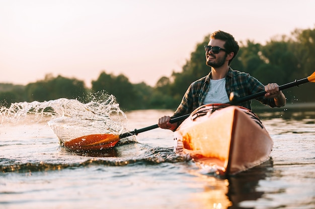 Profiter de la vie sur la rivière. Beau jeune homme souriant aux projections d'eau en kayak sur la rivière