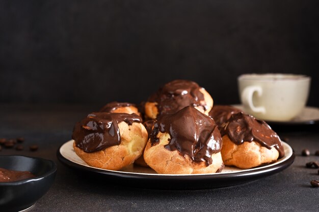 Profiteroles à la crème vanille et sauce au chocolat avec une tasse de café sur la table de la cuisine.