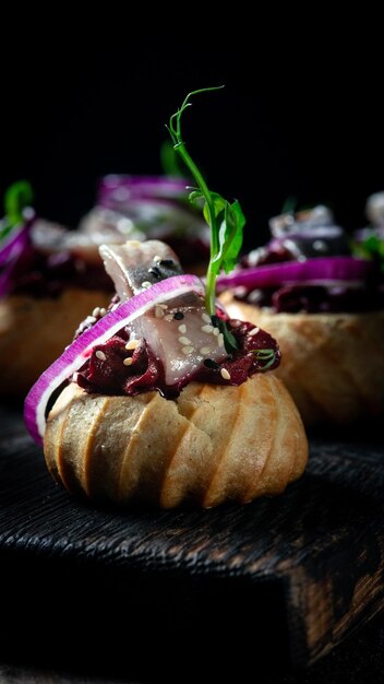 Profiteroles avec du fromage cottage au hareng et de l'oignon rouge sur un fond sombre