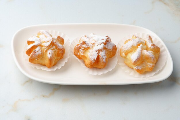 Profiteroles maison avec du sucre en poudre sur plaque blanche