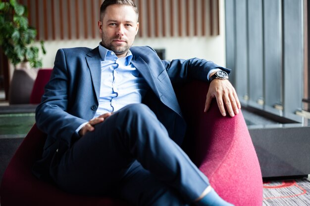 Profitez de chaque jour de votre vie. Homme d'affaires positif et affirmé assis sur le canapé tout en se reposant au bureau, beau fait une pause dans le hall de l'hôtel