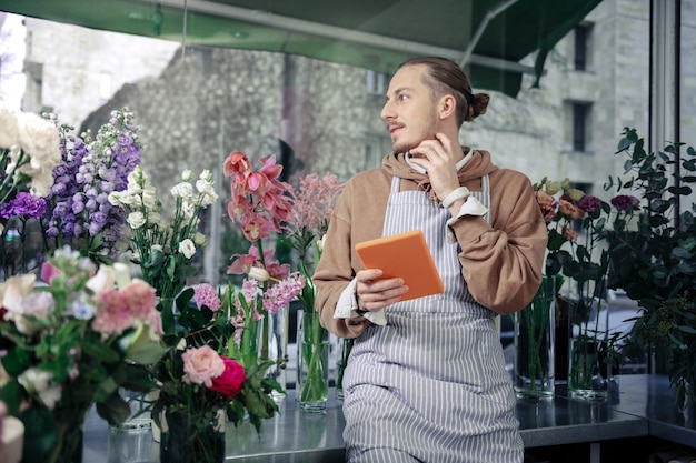 Profondément dans ses pensées. Gentil fleuriste ayant une pause, regardant de côté