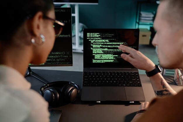 Programmateur informatique masculin pointant vers l'écran de l'ordinateur portable discutant avec un collègue de code sur le lieu de travail