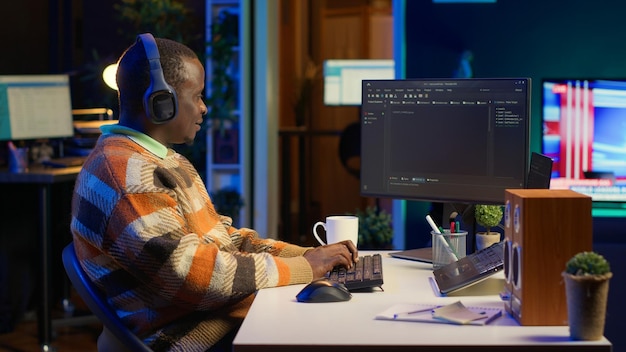 Programmateur noir travaillant à distance dans un bureau à domicile écrivant du code sur un ordinateur