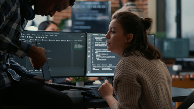 Programmeur junior assis sur un bureau montrant un ordinateur portable avec le code source à un développeur senior demandant son avis. Algorithme d'écriture du développeur de logiciels interrompu par un collègue qui souhaite obtenir de l'aide pour corriger les erreurs.