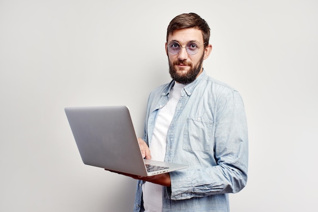 Programmeur masculin caucasien élégant dans des verres, une chemise et avec un ordinateur portable dans ses mains isolé sur un fond de mur blanc