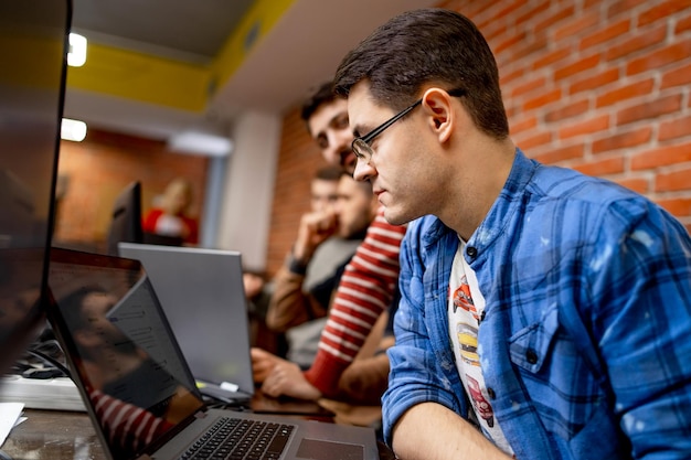 Programmeur masculin travaillant sur un ordinateur de bureau près d'un moniteur au bureau d'une société de développement de logiciels Technologies de programmation et de codage de conception de sites Web