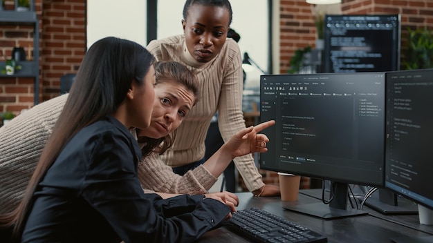 Photo programmeur pointant vers l'écran de l'ordinateur expliquant l'exécution du code aux collègues qui réfléchissent à des idées de logiciels dans une agence indépendante. equipe mixte d'ingénieurs logiciels collaborant sur un projet de groupe informatique.