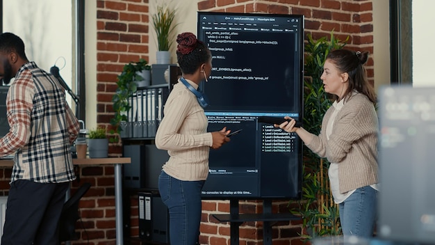Programmeur tenant une tablette numérique analysant le code sur la télévision à écran mural pendant que son collègue recherche des erreurs de pointage à l'aide de la télécommande. Équipe de développeurs d'applications collaborant sur un projet de groupe Big Data.