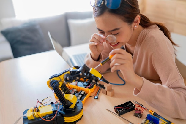 Programmeuse asiatique intelligente apprenant le câble de la carte électronique de codage ai du bras de robot dans STEM STEAM, elle essaie de tester son bras robotique autonome avec des capteurs via la plate-forme Arduino à la maison