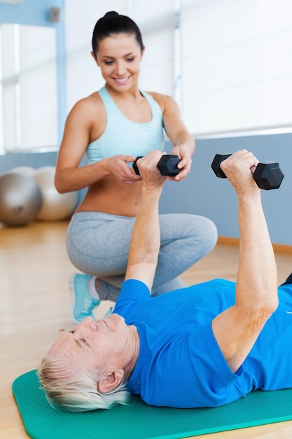 Progresser de jour en jour. Physiothérapeute féminine confiante soutenant un homme âgé dans des exercices de musculation