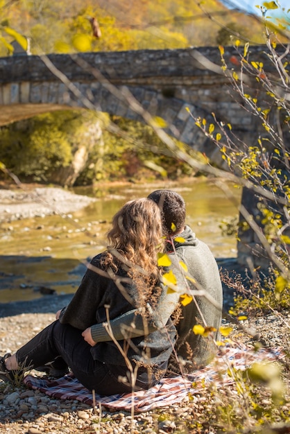 Promenade d'automne. Vue arrière. du couple est assis sur la rive du fleuve. Homme et femme en vêtements chauds regardant une vue d'automne