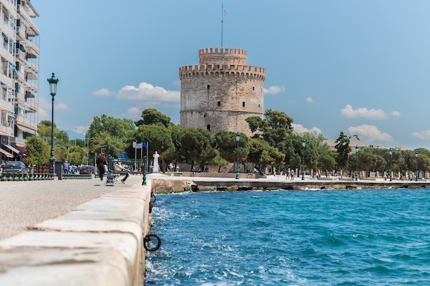 Une promenade en bord de mer à Thessalonique avec une tour blanche du patrimoine byzantin derrière des arbres