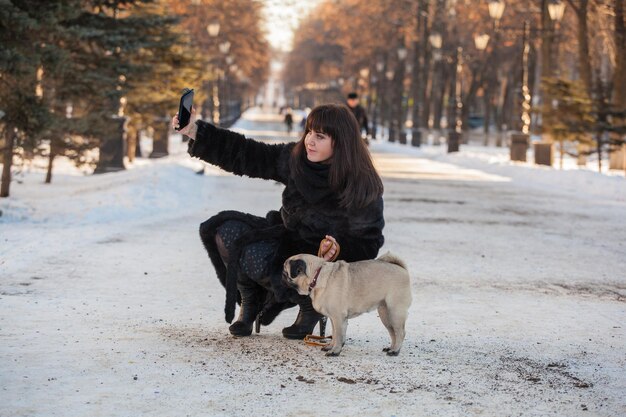 Promenade hivernale dans le parc avec un chien carlin Prenez des photos de vous et du chien sur votre téléphone